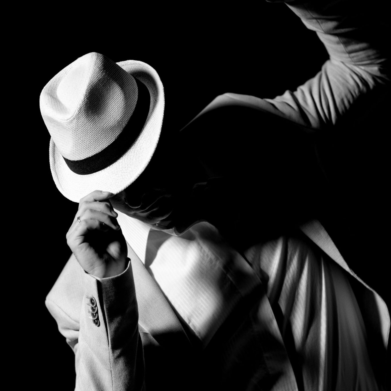 VISUELROUGE – Agence de communication et design graphique Homme en costume blanc et chapeau, dans une pose expressive sur fond sombre.